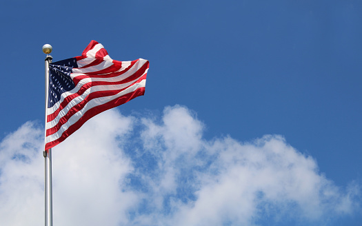 Flying American Flag in blue sky with wispy clouds. Space for copy at top right