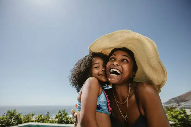 Woman wearing hat enjoying summer vacation with her daughter. African woman with her daughter having fun at the poolside.