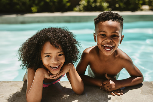 Closeup of cheerful small boy and girl enjoying in swimming pool. Cute brother and sister leaning on pool edge and smiling.