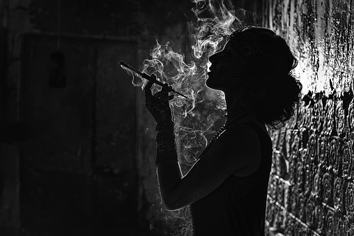 A Black and white silhouette portrait of a young woman smoking a cigarette in a mouthpiece