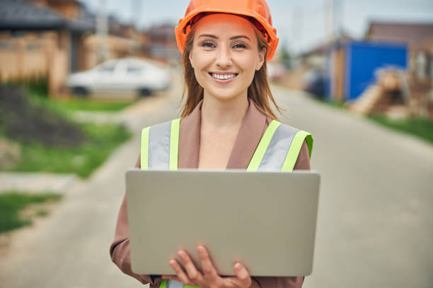 istock Cheerful lady in a protective helmet holding a laptop 1265683617
