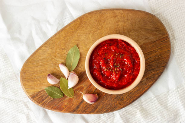 Ajvar in a bowl, garlic and spicy leaves on a wooden board. Serbian traditional food. Ajvar, balkan traditional sauce in a bowl, garlic and spicy leaves on a wooden board. Serbian traditional food. Top view. relish stock pictures, royalty-free photos & images