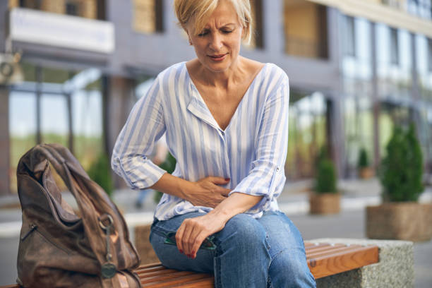 Mature Caucasian lady experiencing a severe stomachache Front view of a frustrated woman suffering from an acute abdominal pain on the bench stomachache stock pictures, royalty-free photos & images