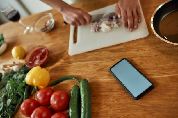 istock Close up of phone with blank screen on the table. Man cutting onion on chopping board, using smartphone app while cooking dinner. Healthy nutrition, technology concept 1265695081