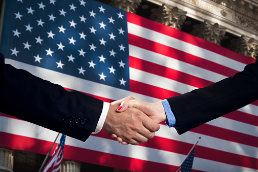 People shake hands and make an agreement in front of the American flag