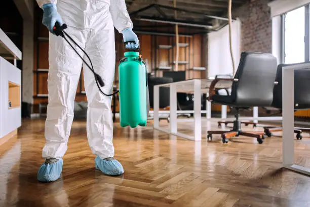 Man in protective suit spraying for disinfection in the office