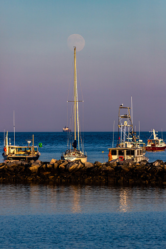 Full moon rising above large boat and rocks in the ocean. in Rye, NH, United States