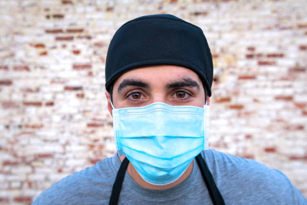 istock Serious Pensive Restaurant worker wearing a protective face mask looking at the camera 1265712915