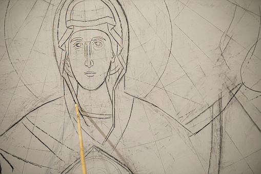 The young artist begins painting the wall of the Orthodox Church by sketching a fresco of the Virgin Mary