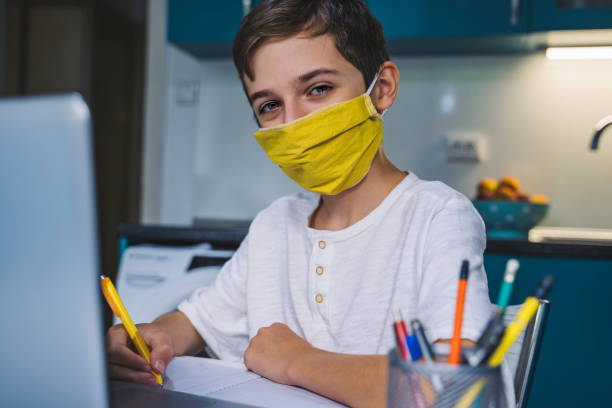 istock Back to school. Cute boy with face protective mask studying at home. Online education. Coronavirus epidemic. Covid-19. Copy space. 1265722100