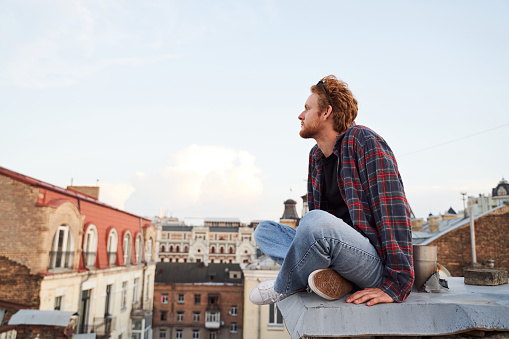 Cakm handsome guy is meeting morning on roof of urban building while sitting on edge