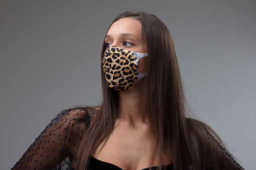 Woman wearing a textile patterned face mask with animal print during the Covid-19 pandemic as protection against coronavirus looking to the side in a stylish black top