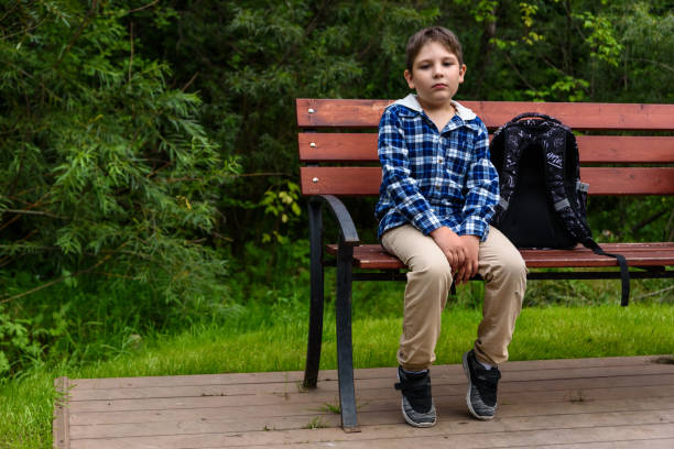istock Sad school boy with backpack sitting on a street bench and thinking 1265739119