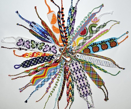 Many woven handmade friendship bracelets with bright colorful pattern made of embroidery thread on white background. They are laid out in a circle