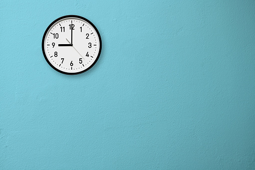 Wall clock on the blue wall with copy space.\n9 o'clock