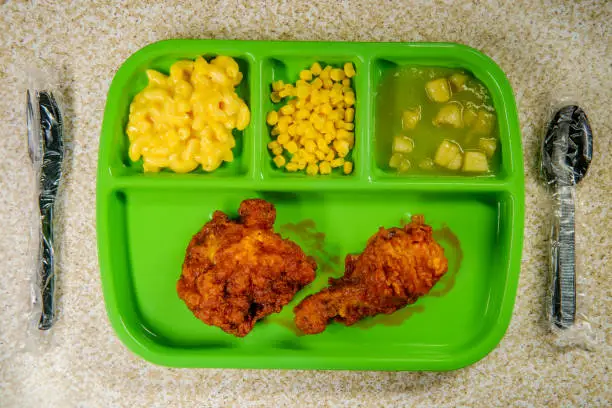 Grade school lunch tray of deep fried chicken legs with macaroni and cheese corn and apple sauce
