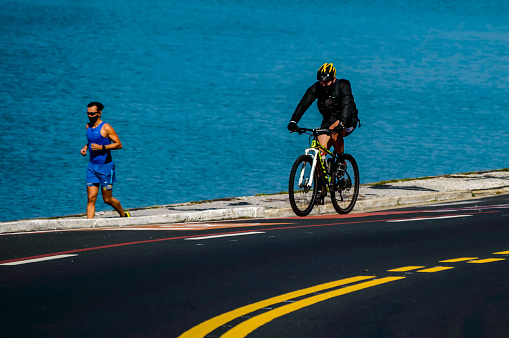 Florianopolis, Santa Catarina, Brazil. August 8, 2020: A cyclist and a runner on the edge of the sea.