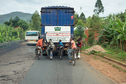 Bujumbura / Burundi - October 15, 2016: group of young men riding bicycle while towed by large truck in beautiful mountain road