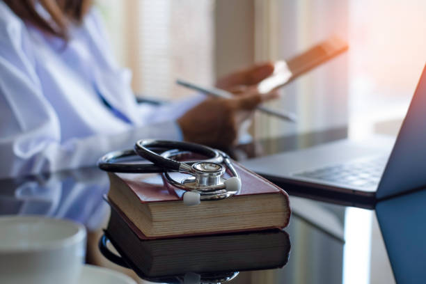 Female doctor Female doctor hand holding clipboard, read patient medical health report information with laptop computer, text book and medical stethoscope on the dark mirror desk at office. medical journal stock pictures, royalty-free photos & images