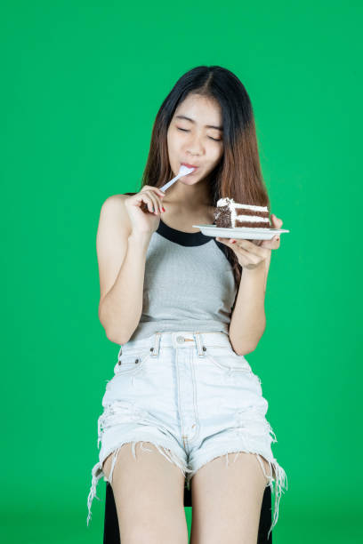 felice deliziosa ragazza asiatica che mangia torta al cioccolato su sfondo verde isolato. - thai cuisine asian cuisine vertical close up foto e immagini stock