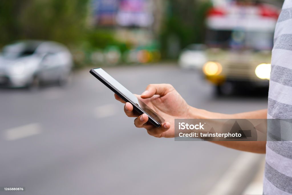 Hand of man using a mobile phone on the street. Use of transportation app Crowdsourced Taxi Stock Photo