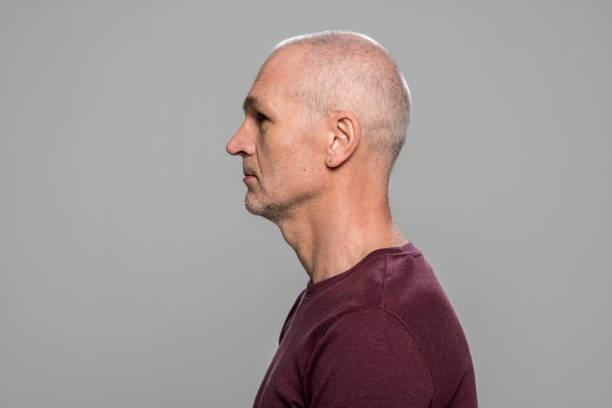 Close-up of mature man Profile of mature man in maroon t-shirt standing against grey background. balding photos stock pictures, royalty-free photos & images