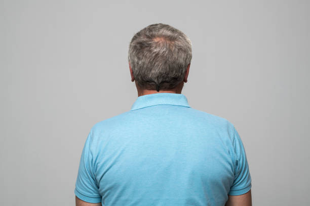 Rear view of senior man in blue polo shirt standing against grey background.