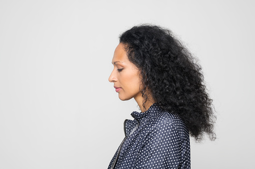 Profile of woman in blue spotted jacket looking down while standing against grey background.