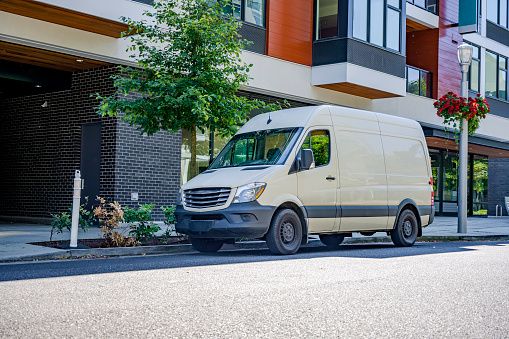 Compact cargo mini van for delivery and small business services standing on the urban city street with urban multi level residential apartment building