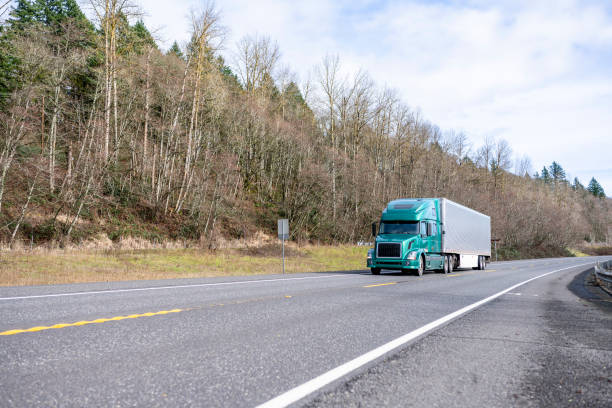 istock Green bonnet big rig semi truck transporting cargo in refrigerator semi trailer driving on the road with forest on the hill side 1265922015