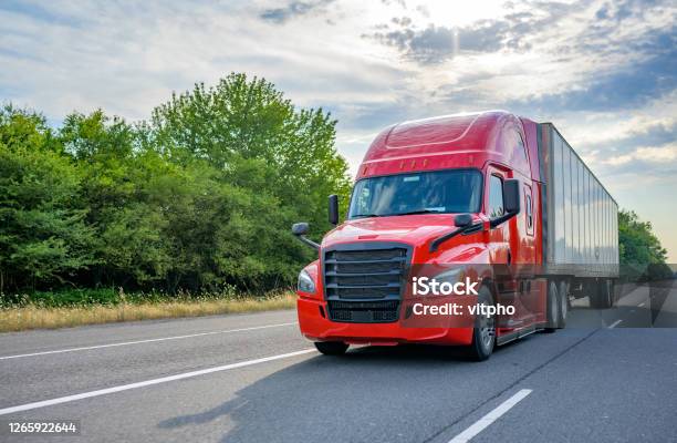 Red Big Rig Long Haul Semi Truck With Black Grille Transporting Cargo In Dry Van Semi Trailer Running On The Wide Highway Road Stock Photo - Download Image Now