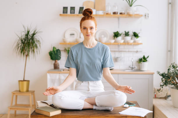 a jovem ruiva sorridente está meditando enquanto está sentada na mesa do home office, olhando para a câmera. - looking at camera smiling desk isolated - fotografias e filmes do acervo