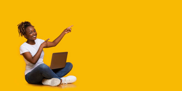 istock Black girl with laptop pointing at empty space 1265924357