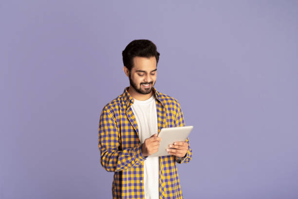 istock Smiling Indian man studying or working online on tablet computer over lilac background 1265926605