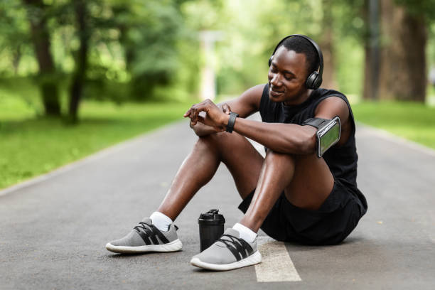 istock Athletic black man sitting on park way, checking on smartwatch 1265927128