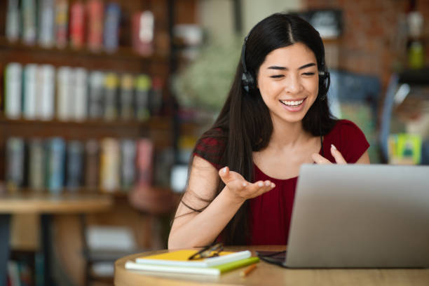 Smiling asian woman in headset having video conference on laptop Smiling asian woman in headset having video conference on laptop, sitting at city cafe, selective focus, free space online tutors stock pictures, royalty-free photos & images