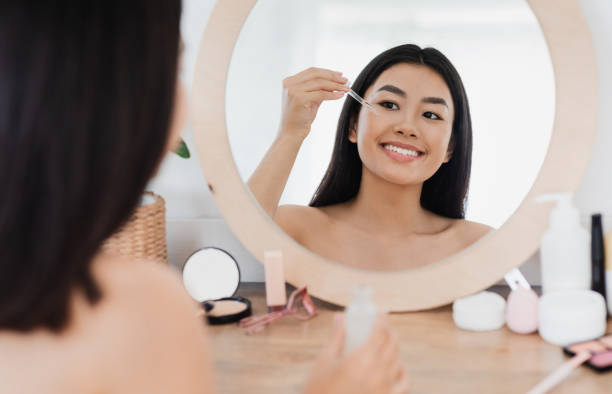 Happy asian girl applying eye serum at home Eye zone care concept. Happy beautiful asian girl applying eye serum in front of mirror at home blood serum photos stock pictures, royalty-free photos & images