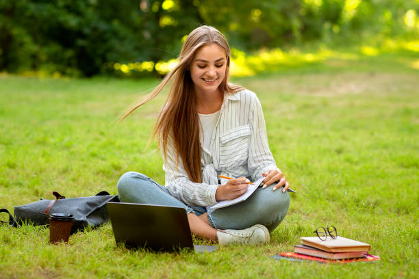 istock Beautiful student girl preparing for lessons in park, writing notes to workbook 1265944577
