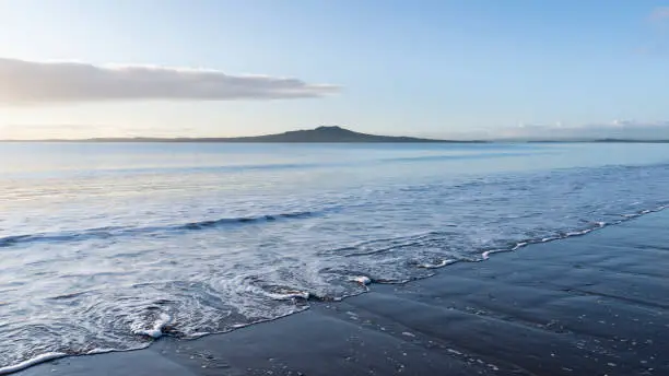 Photo of Milford beach at sunrise with swirl waves in the foreground and Rangitoto Island in the distance