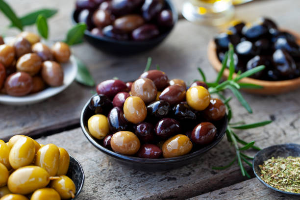 Assortment of fresh olives on a plate with olive tree brunches. Wooden background. Close up. stock photo