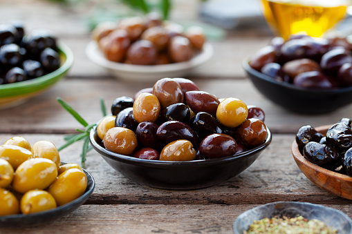 Assortment of fresh olives on a plate with olive tree brunches. Wooden background. Close up.