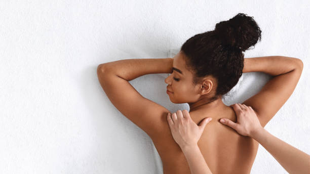 mani massaggiatrici che sfregano le spalle della donna africana sul bianco - massaggiatore foto e immagini stock