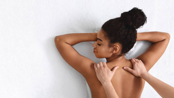 istock Masseuse hands rubbing african woman shoulders over white 1265951858