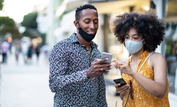 istock Afro Couple wearing protective face mask walking on the streets and using smart phone, during COVID-19 1265954008