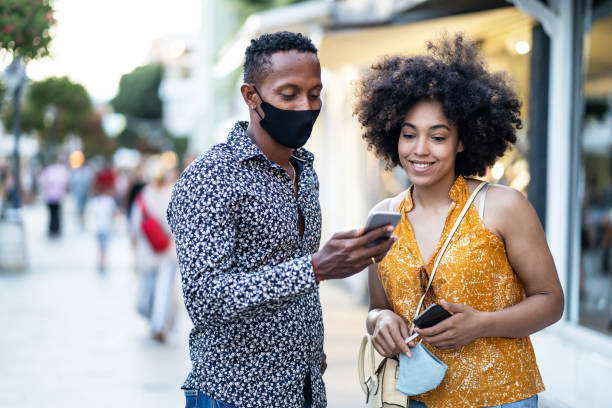istock Afro Couple wearing protective face mask walking on the streets and using smart phone, during COVID-19 1265954009
