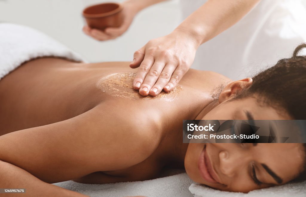 Masseuse applying body scrub on black girl back Beauty procedures at spa. Masseuse applying body scrub on black girl back, closeup Spa Stock Photo