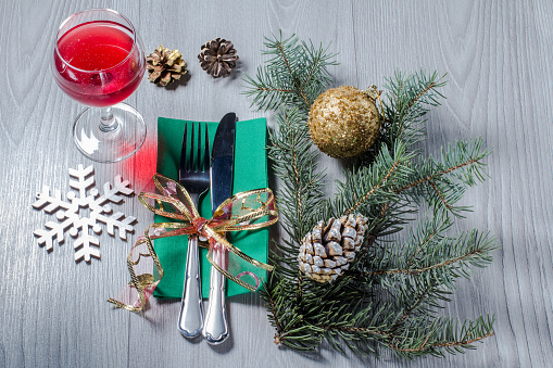 Knife and fork on green napkin with glass of wine, decorative snowflake, cone, glittering ball and natural fir tree branches on wooden boards.  Christmas and New Year cutlery concept