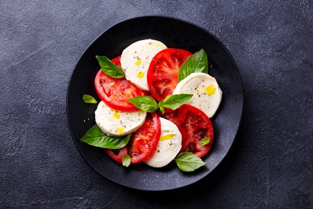 salade de caprese aux tomates, mozzarella, basilic. fond sombre. fermez-vous. vue supérieure. - mozzarella caprese salad tomato italian cuisine photos et images de collection