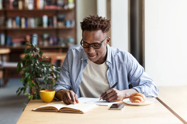istock Focused male student taking notes from textbook at table in coffee shop 1265958291
