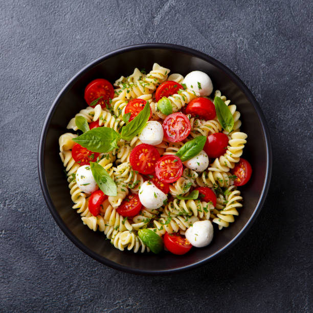 Pasta fusilli with mozzarella cheese, tomatoes and basil. Dark background. Close up. Top view.